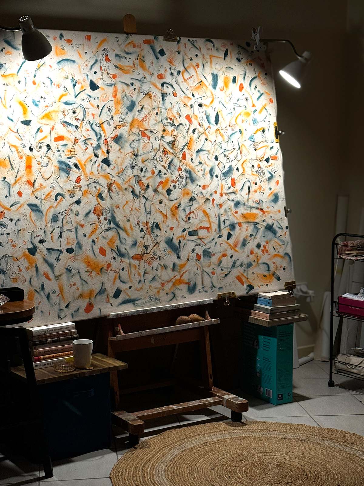 Abstract expressionism artwork on raw cotton canvas. Colours are orange tones, dark and light blue/teal brush strokes. Organic patterns and faces expressing different emotions. Artist studio photo. Made by Studio Thicia Luiza