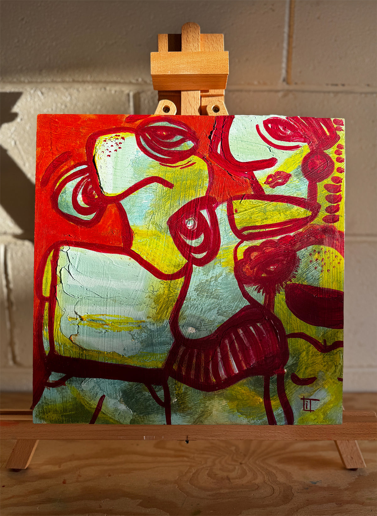 Abstract painting on a wooden easel against a textured wall. In turquoise, green, orange and red by Studio Thicia Luiza